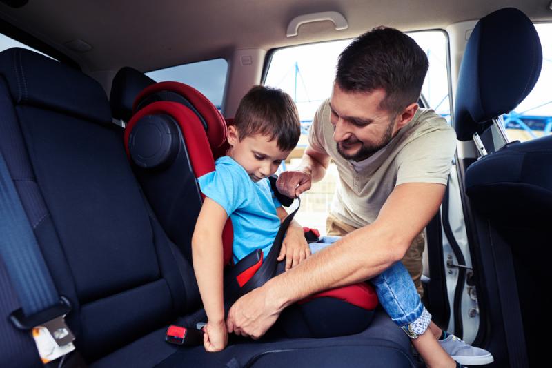 a father helping his kid to set in a car seat